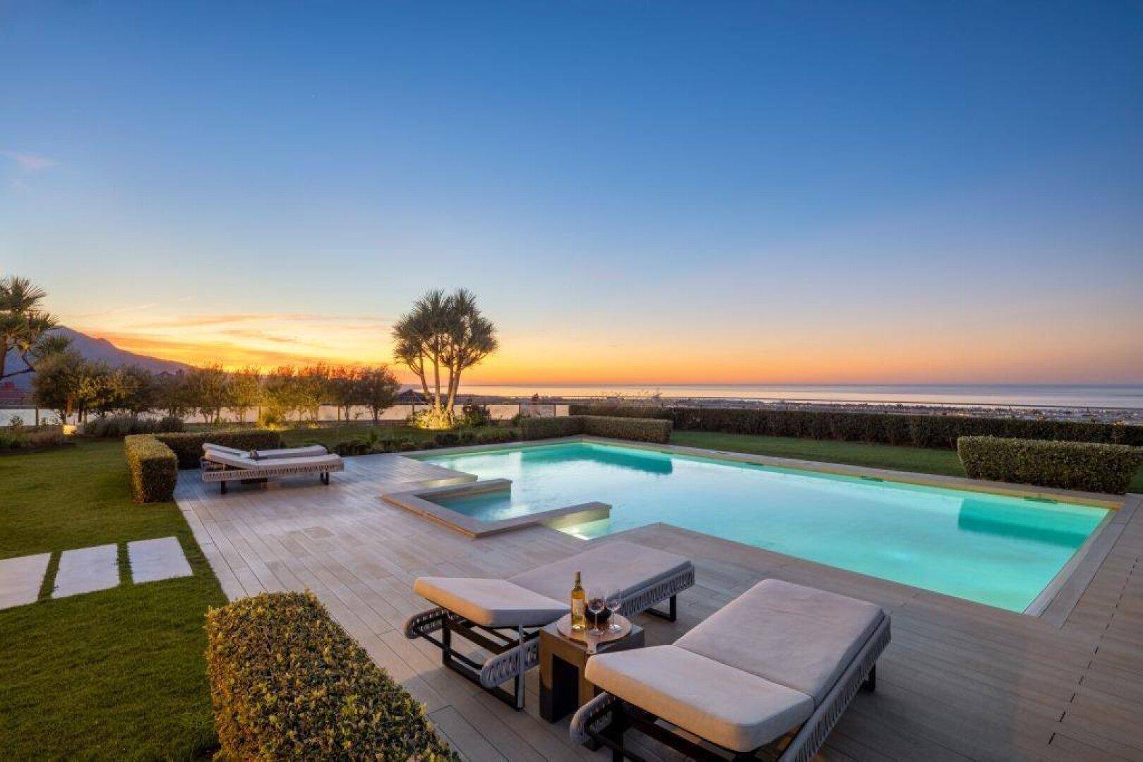 Malerischer Poolbereich bei Sonnenuntergang mit Liegestühlen und Blick auf das Meer.