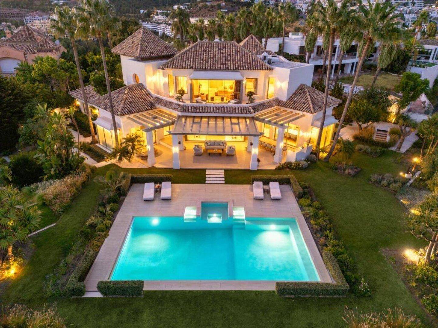 Beeindruckende Luftaufnahme der beleuchteten Villa mit Pool und Garten bei Dämmerung.