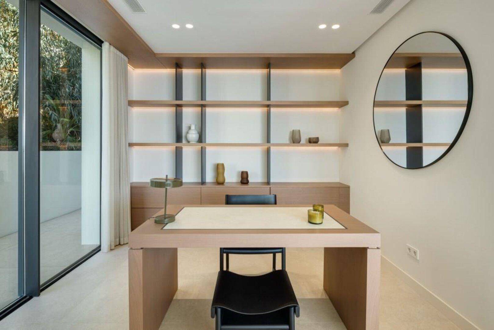 Modernes Arbeitszimmer mit großem Fenster, Holzelementen und integrierten Regalen.