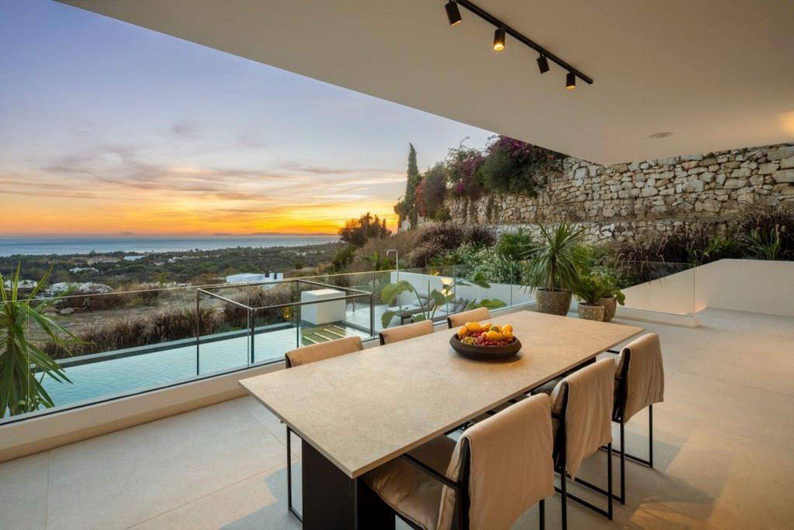 Elegante Terrasse mit Esstisch und atemberaubendem Meerblick bei Sonnenuntergang.