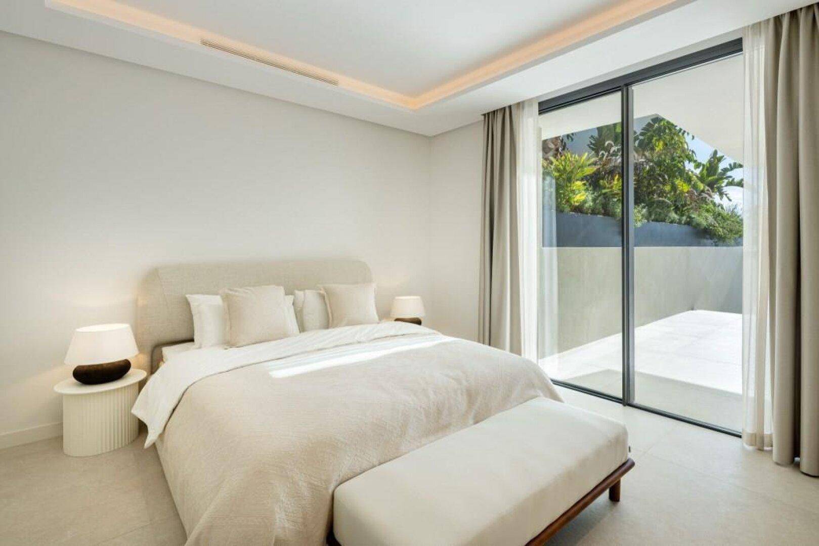 Helles Schlafzimmer mit großem Bett, Zugang zur Terrasse und Blick ins Grüne.