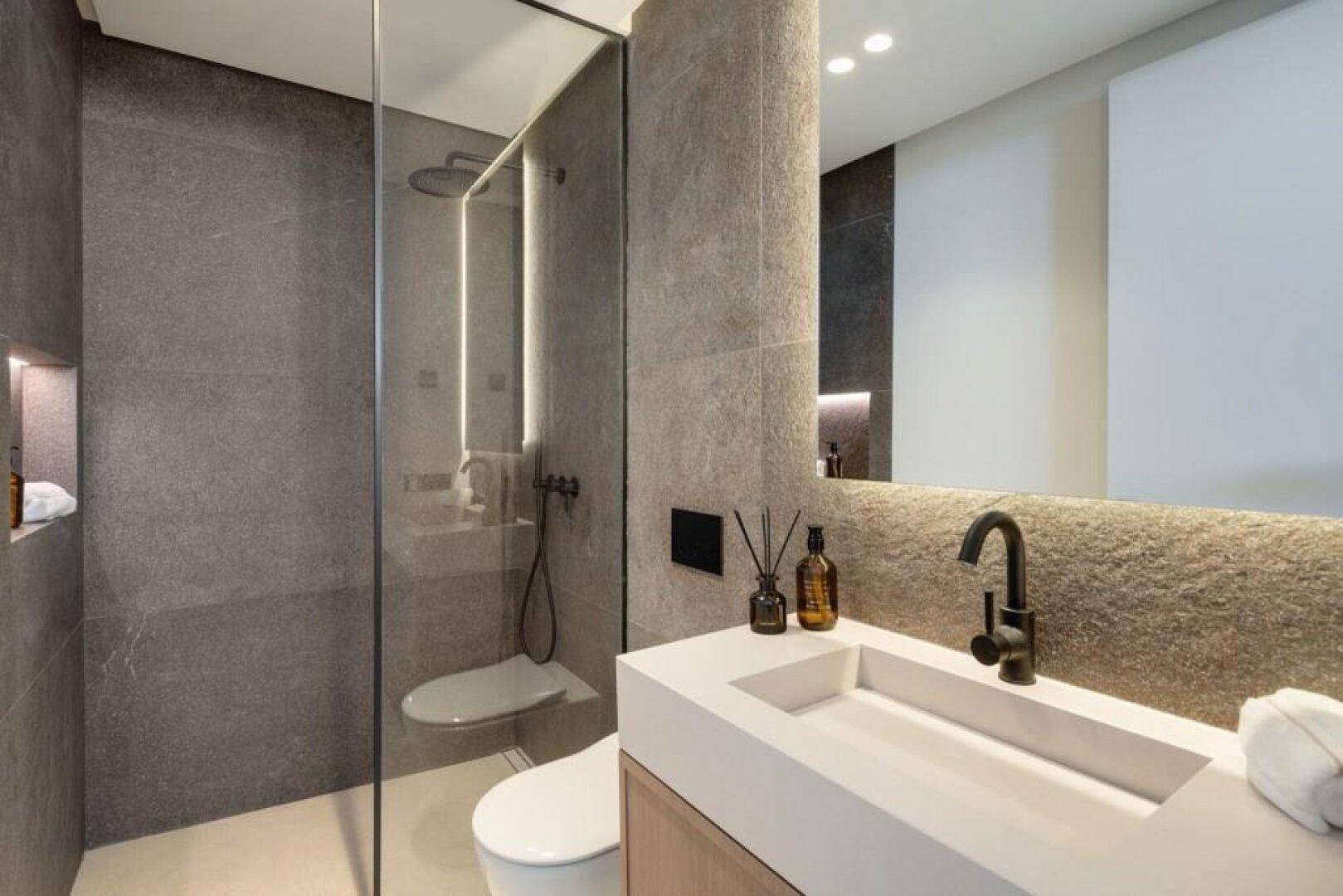 Modernes Badezimmer mit begehbarer Dusche, stilvollem Waschtisch und dunklen Fliesen.