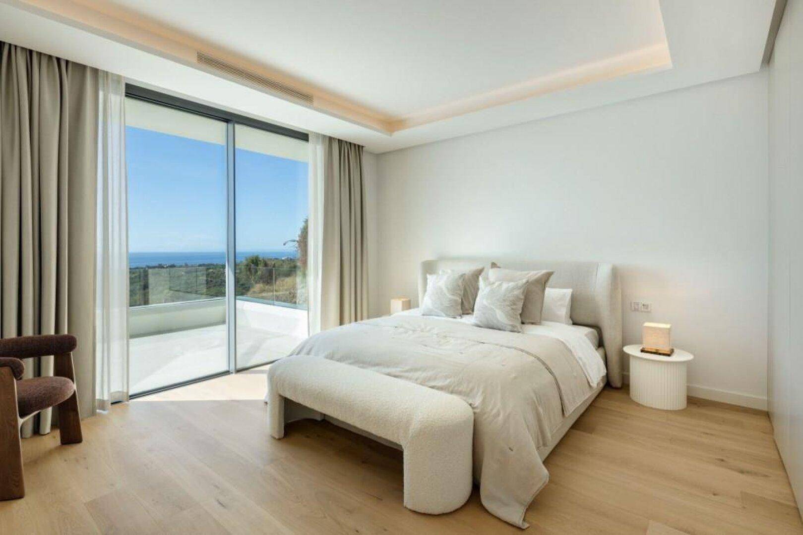 Schlafzimmer mit Meerblick, Holzboden und großen Schiebetüren zur Terrasse.