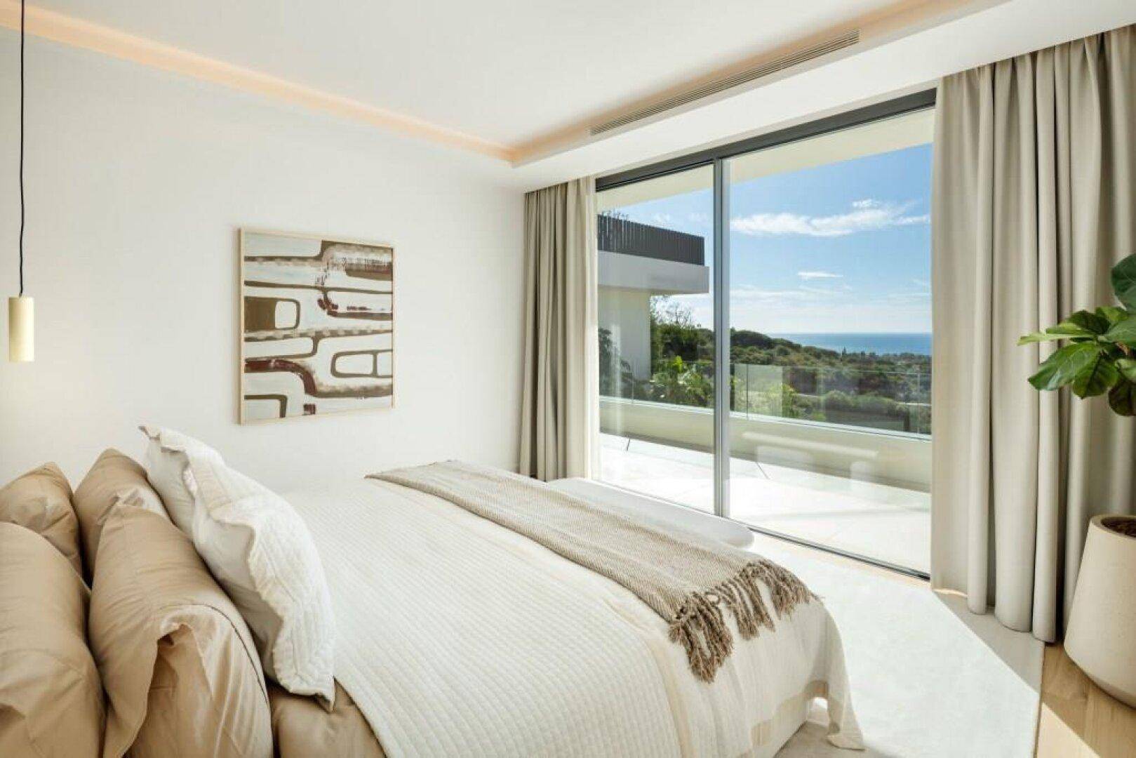 Helles Schlafzimmer mit Meerblick, Holzboden und Zugang zu einem Außenbereich.