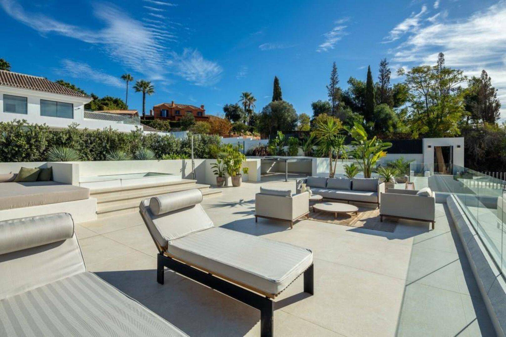 Großzügige Dachterrasse mit Whirlpool-Bereich und vielfältigen Sitzgelegenheiten unter strahlend blauem Himmel.