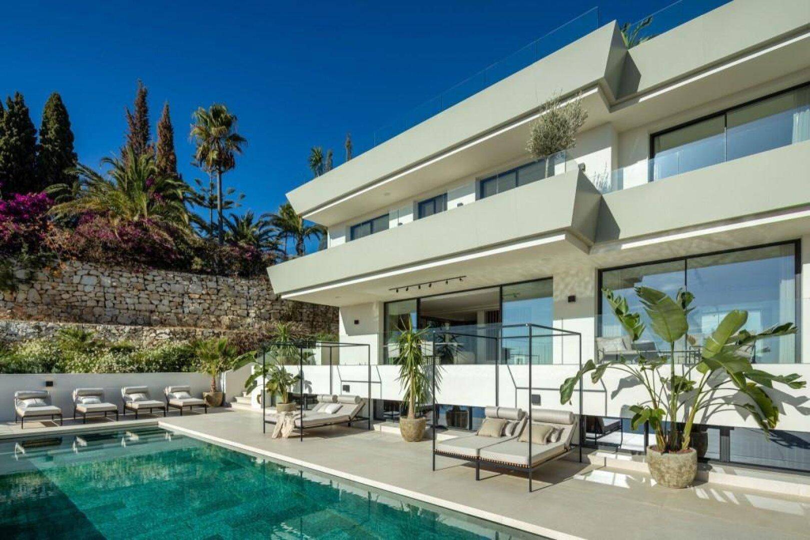 Die moderne Villa mit großem Poolbereich, bequemen Sonnenliegen und üppiger tropischer Bepflanzung.