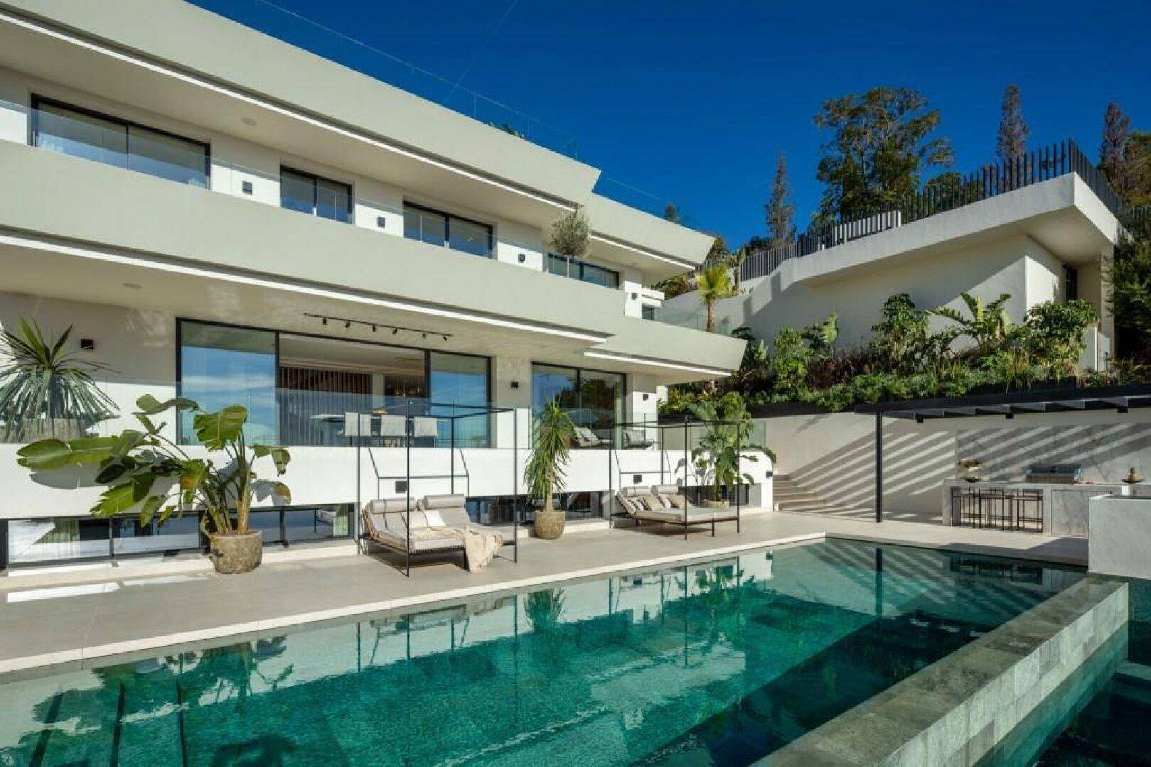 Elegante moderne Villa mit großem Infinity-Pool und weitläufigen Terrassenbereichen unter blauem Himmel.