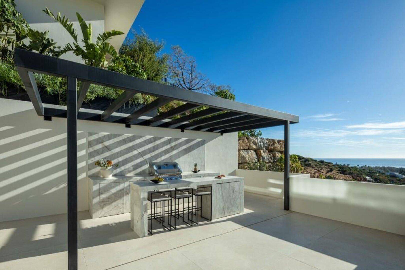 Stilvolle Außenküche mit Grillbereich unter einer Pergola und herrlichem Blick auf das Meer.