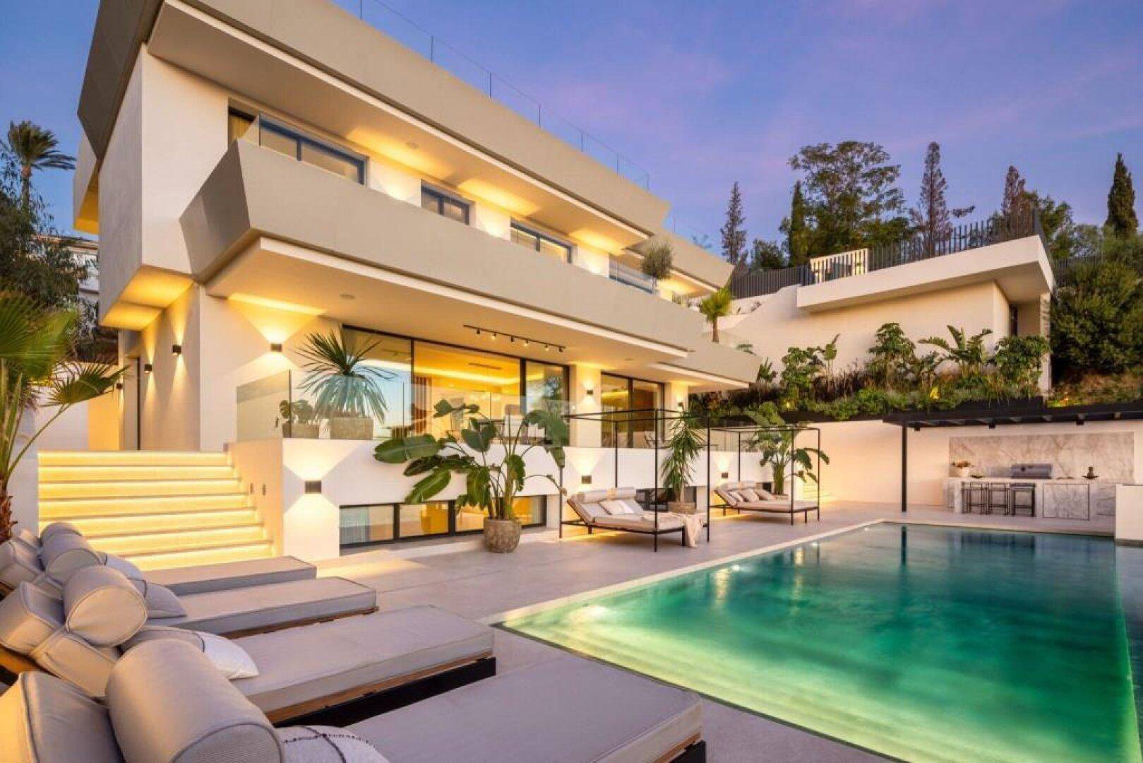 Die luxuriöse Villa bei Dämmerung, mit beleuchteten Treppen, Poolbereich und eleganter Fassadenbeleuchtung.