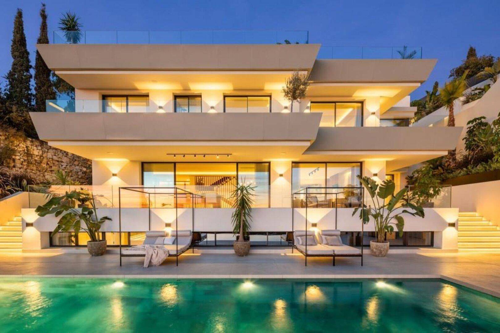 Moderne Villa mit beleuchtetem Poolbereich und luxuriösen Liegen bei Sonnenuntergang.