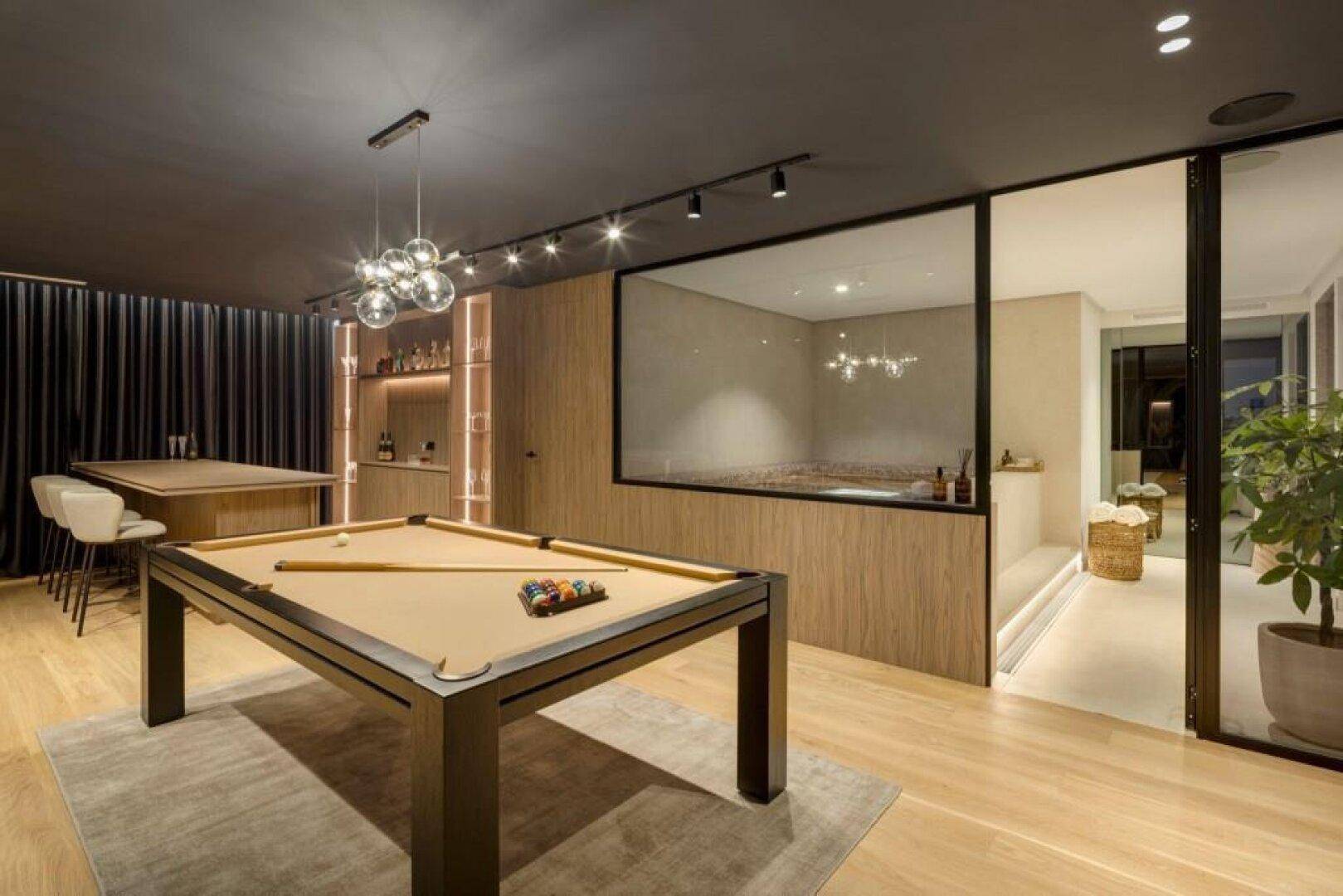 Geräumiger Spielbereich mit Billardtisch und eleganter Bar, angrenzend an einen Wellnessbereich mit Pool.