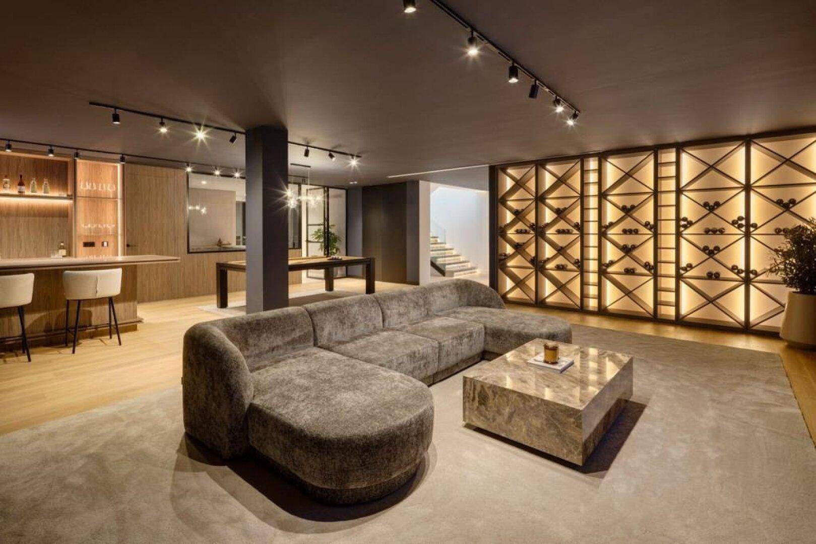 Geräumiges Wohnzimmer mit bequemer Sitzecke, beleuchteter Weinwand und offenem Übergang zum Barbereich.