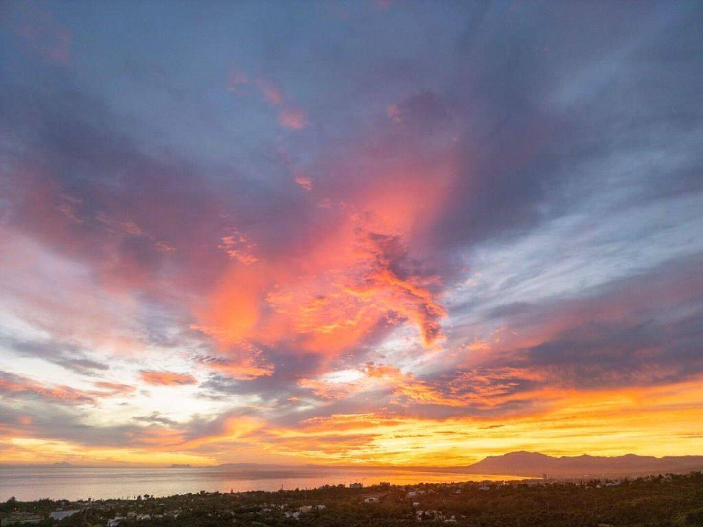 Spektakulärer Sonnenuntergang über dem Meer mit leuchtenden Wolken und Küstenlandschaft.
