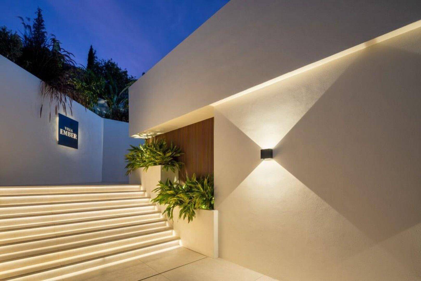 Beleuchteter Eingangsbereich der Villa bei Nacht, mit stilvoller Treppenbeleuchtung und Namensschild.