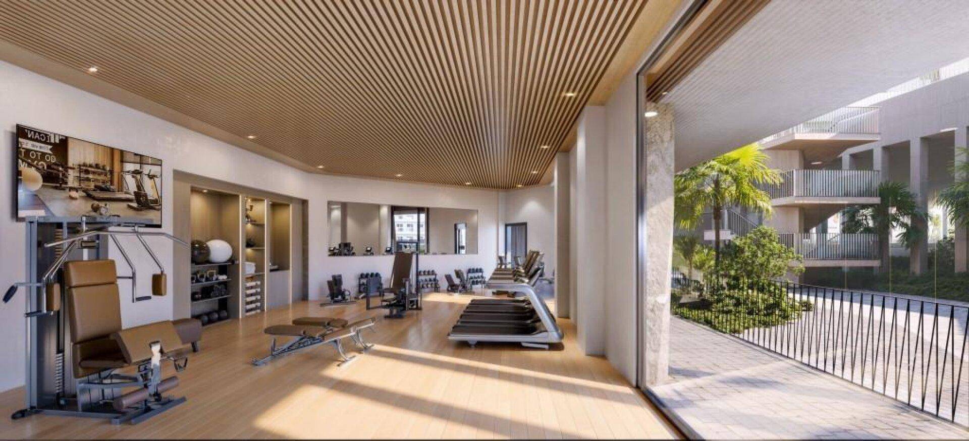 Moderner Fitnessraum mit verschiedenen Trainingsgeräten, großen Fenstern und Blick auf Palmen im Außenbereich.