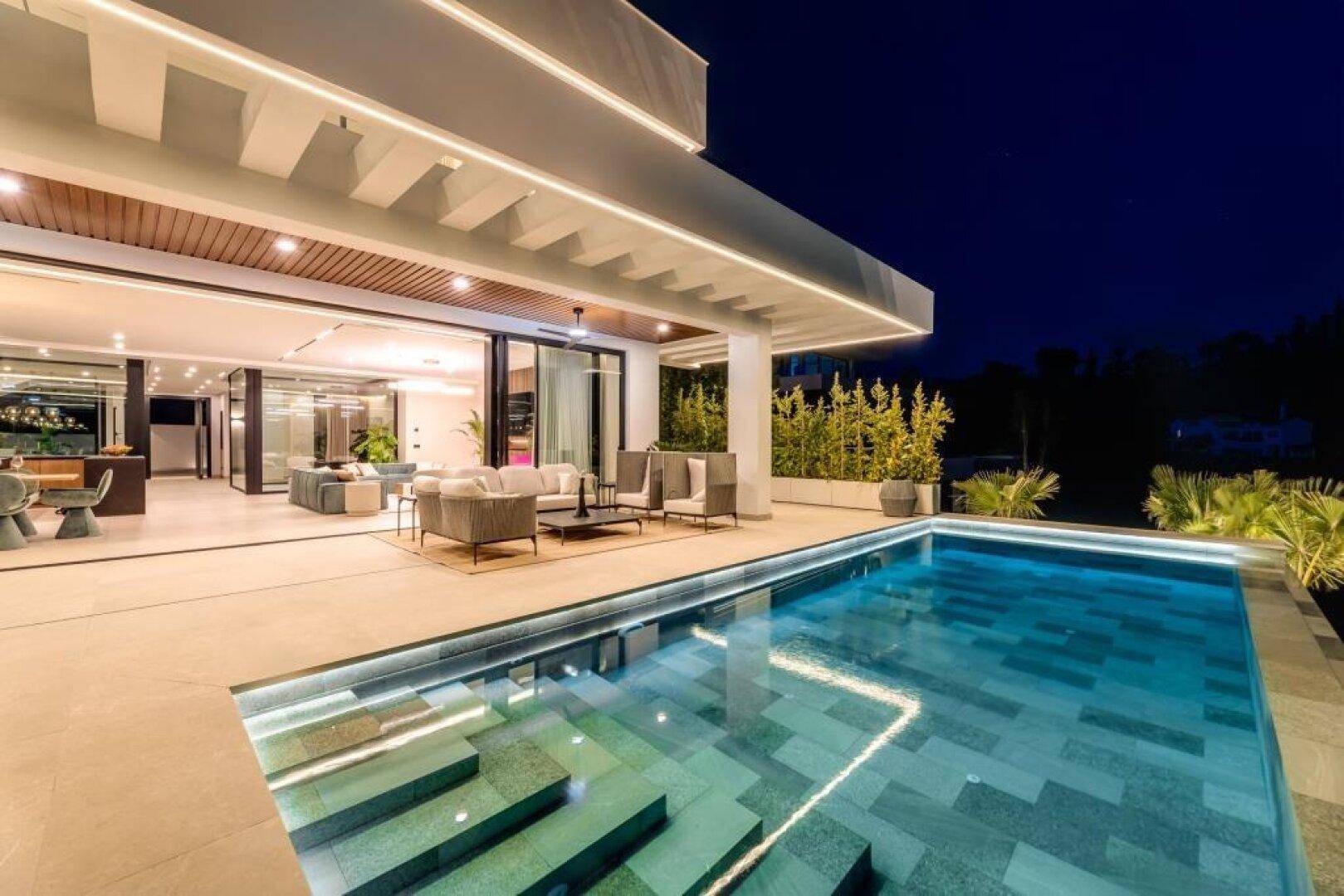 Beleuchtete Terrasse mit Pool und Blick auf den Innenbereich des Hauses bei Nacht.