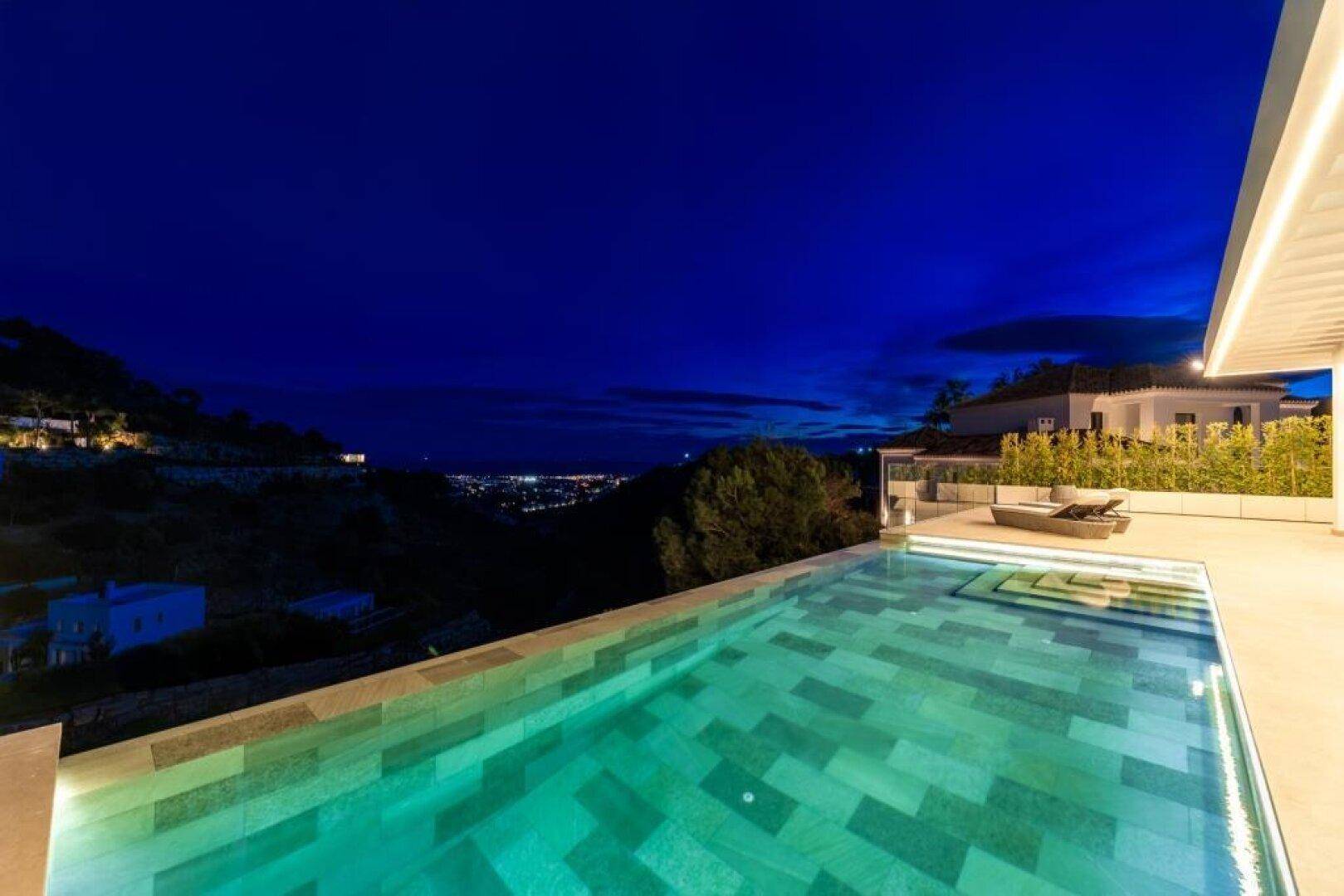 Infinity-Pool bei Nacht mit beeindruckendem Blick auf die beleuchtete Stadt und das Meer.