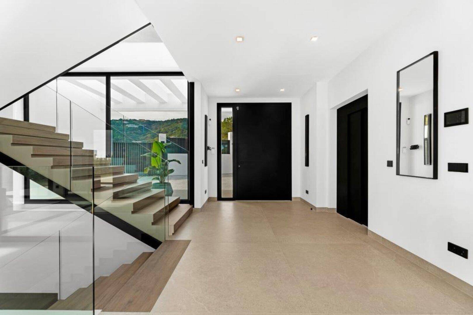 Heller Eingangsbereich mit moderner Treppe aus Holz und Glas sowie großen Fenstern.