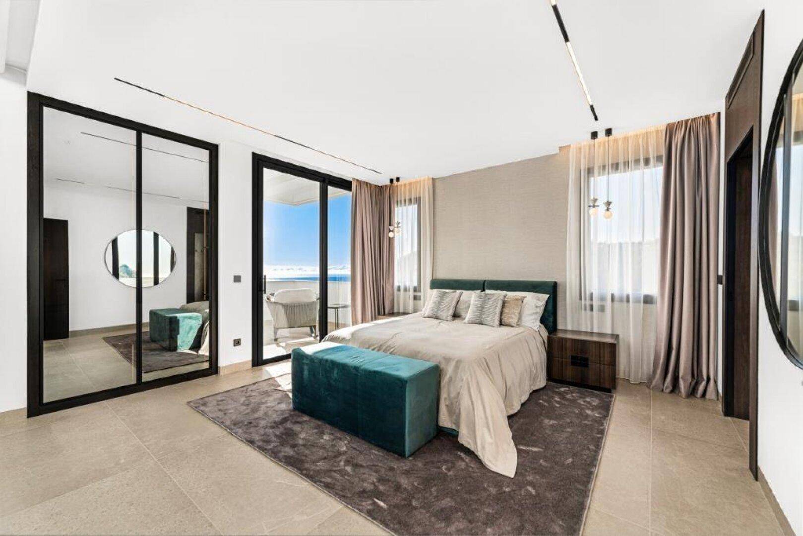 Modernes Schlafzimmer mit großem Bett, Spiegelschränken und Zugang zum Balkon mit Meerblick.