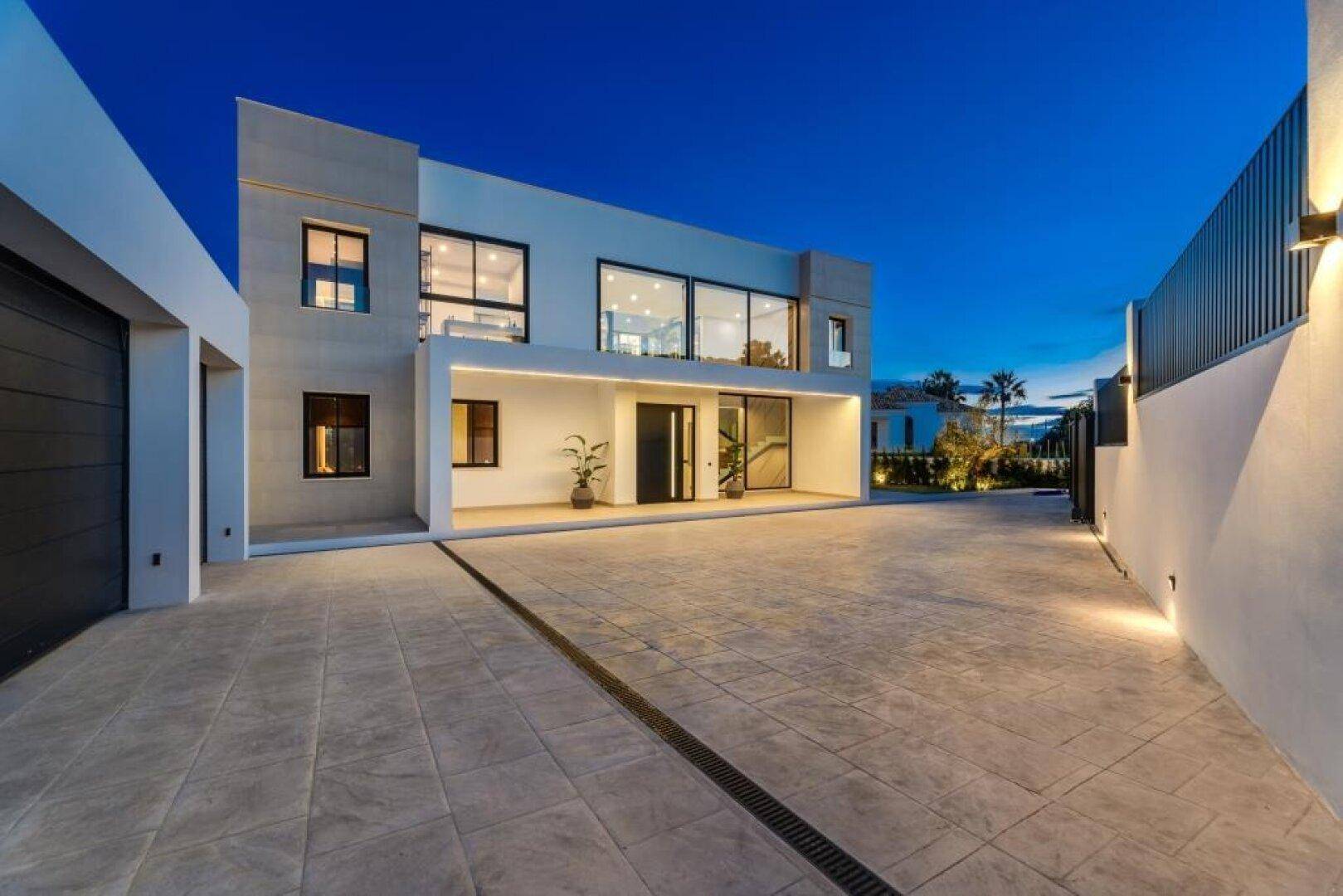 Moderne Villa bei Sonnenuntergang mit großer Auffahrt und Doppelgarage, elegant beleuchtet.