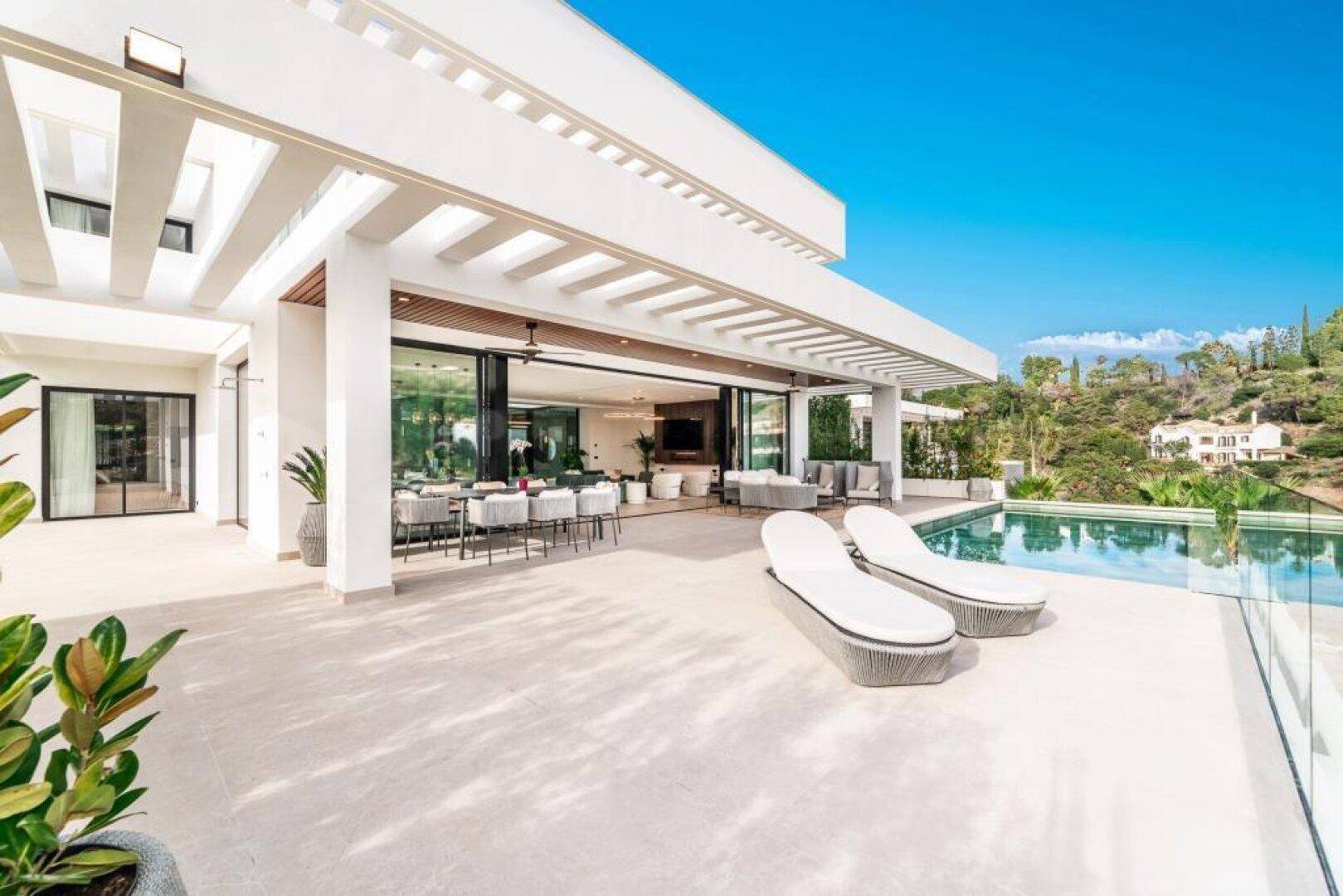 Großzügige Terrasse mit Infinity-Pool, Sonnenliegen und Essbereich im Freien, umgeben von Natur.