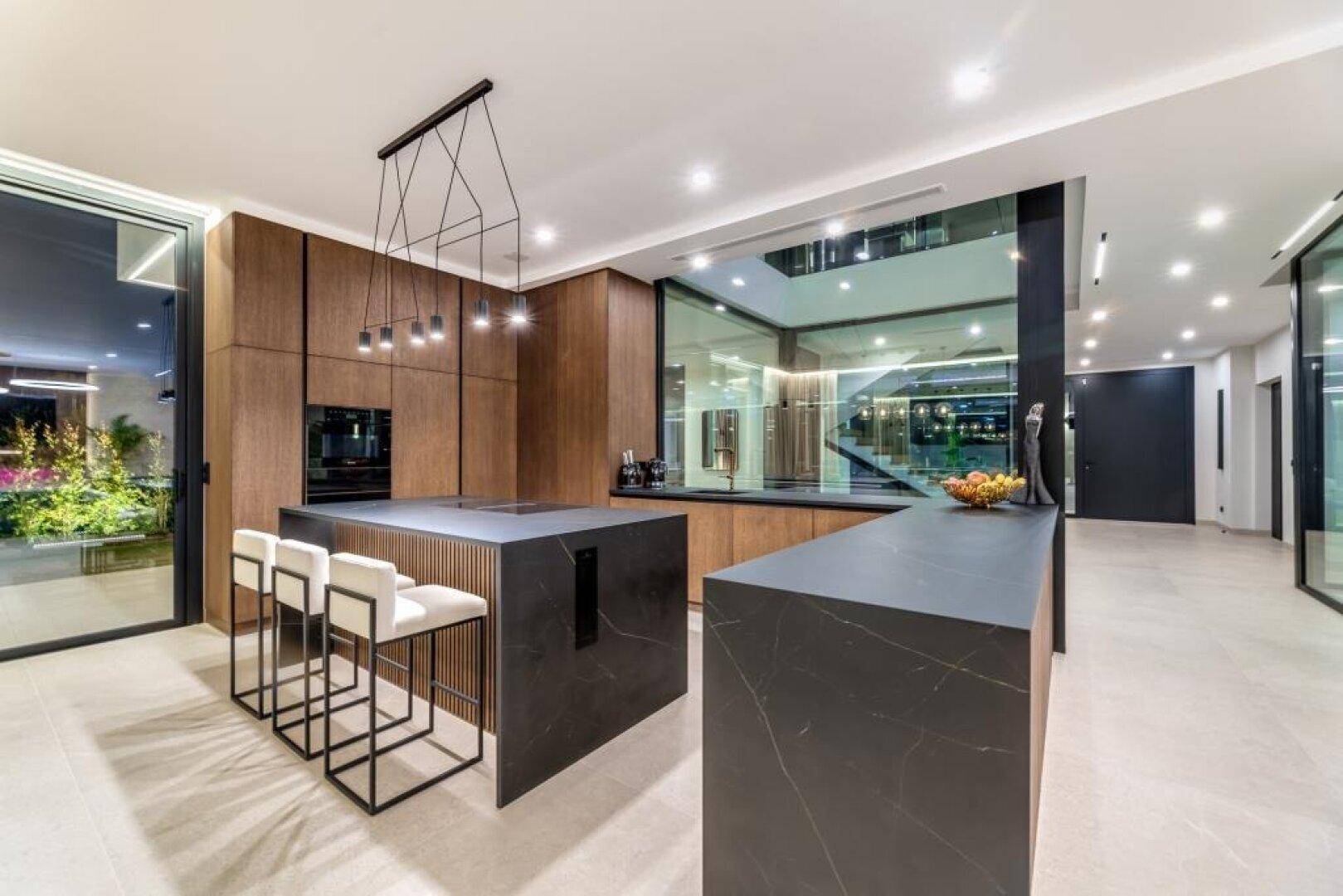 Elegante moderne Küche mit dunklen Arbeitsplatten und Holzschränken, offen gestaltet und hell.