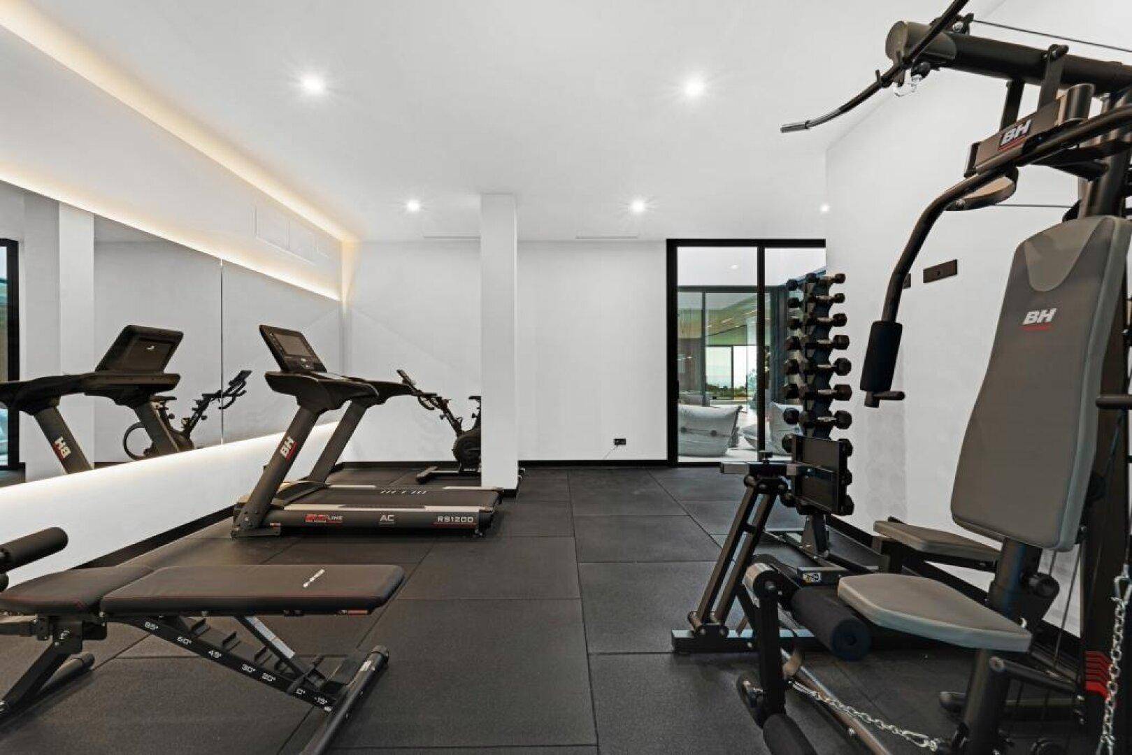 Gut ausgestatteter Fitnessraum mit Laufbändern, Hanteln und großem Spiegel für das tägliche Training.