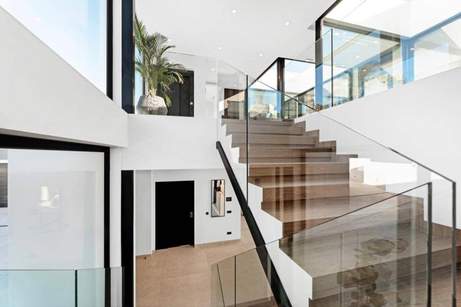 Elegante moderne Treppe mit Glasgeländer und Holzstufen in einem lichtdurchfluteten Raum.