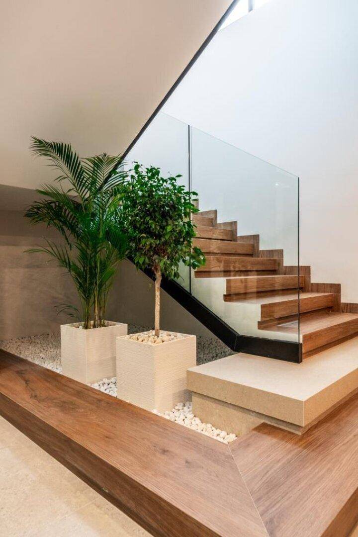 Moderne Holztreppe mit Glasgeländer und dekorativen Pflanzen in einem hellen, offenen Bereich.