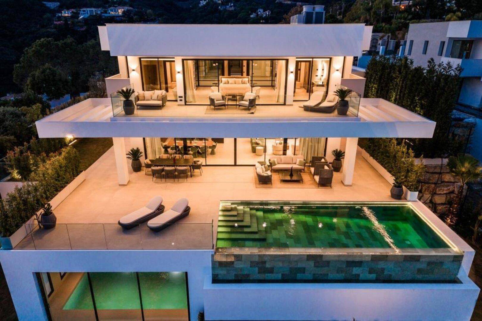 Beeindruckende moderne Villa bei Nacht mit beleuchteten Terrassen und Pool, luxuriös und einladend.