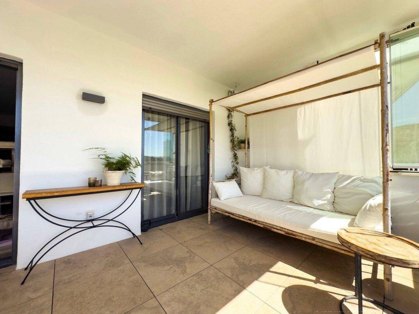Helle Terrasse mit Tagesbett und Beistelltischen, ideal zum Entspannen im Freien.