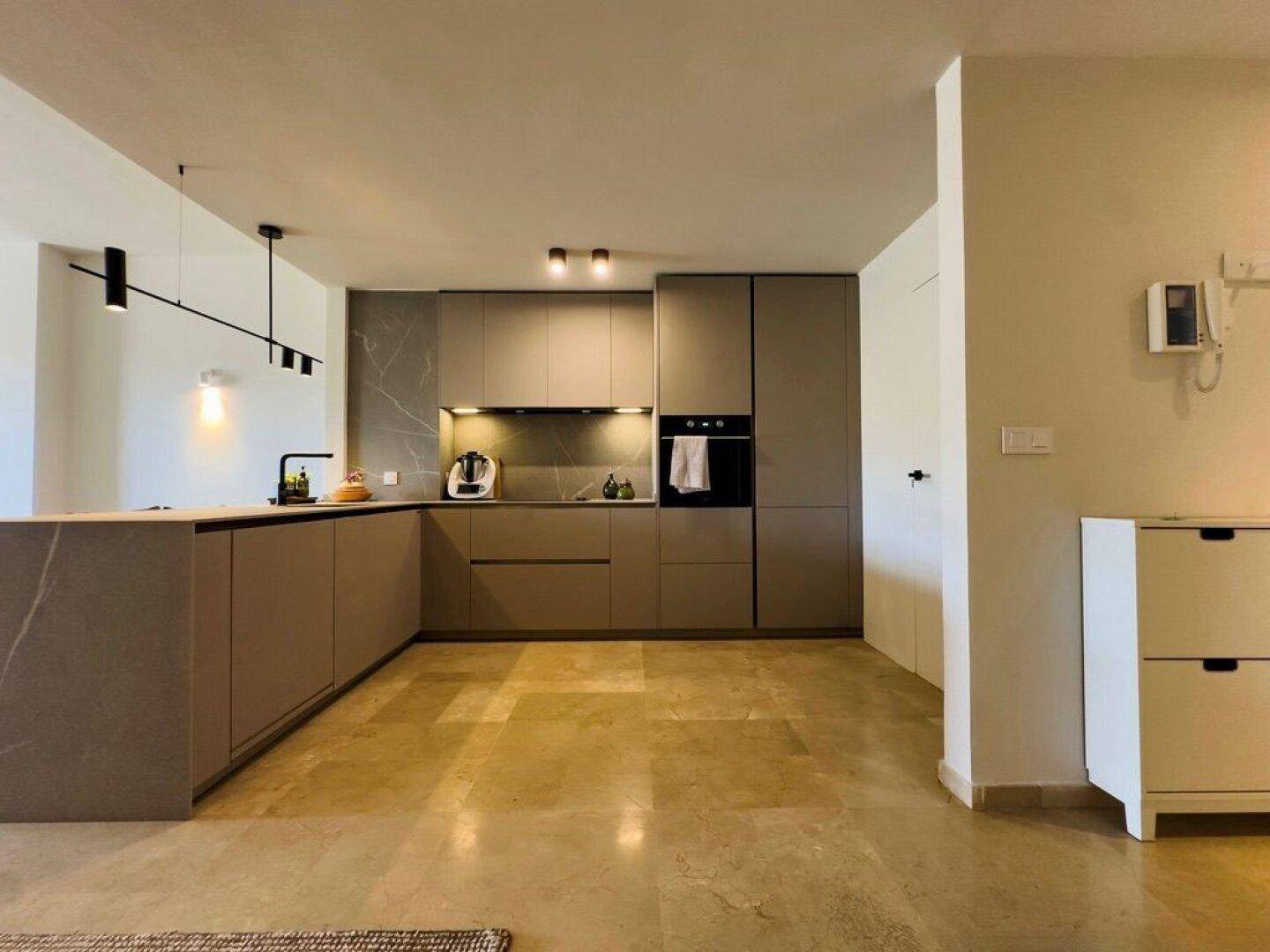 Moderne Einbauküche in Grau mit integrierten Geräten und Fliesenboden.