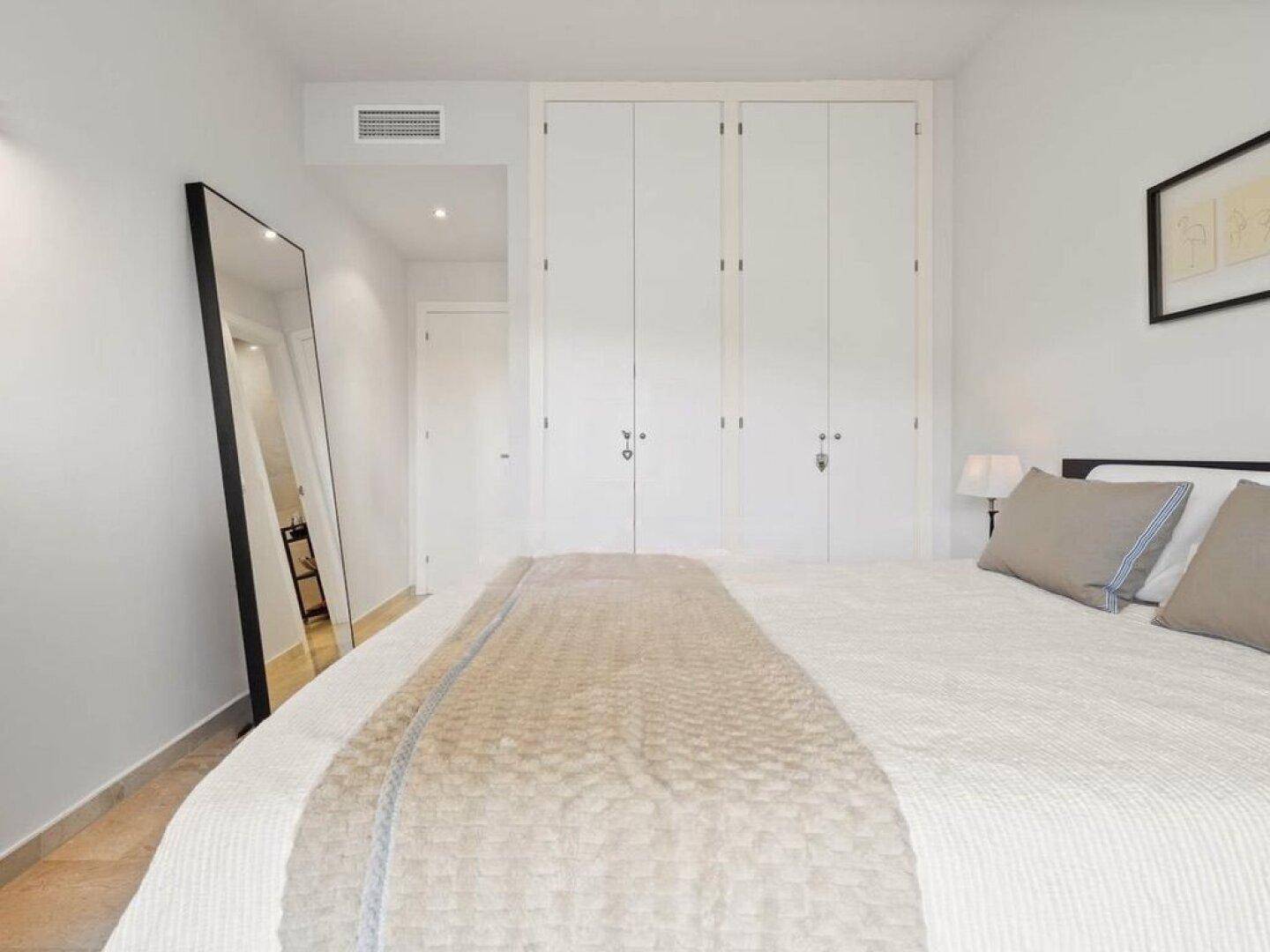 Schlafzimmer mit großem Spiegel und Einbauschränken, in neutralen Farben gehalten.