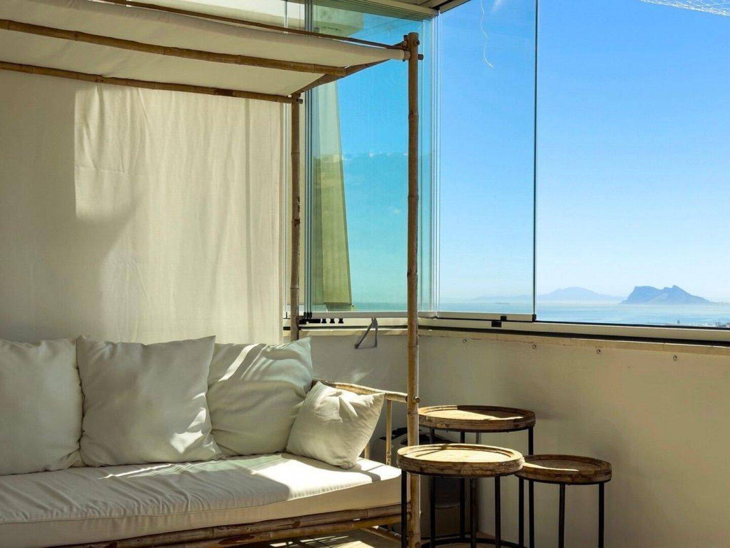 Verglaste Terrasse mit Tagesbett und weitem Meerblick unter blauem Himmel.