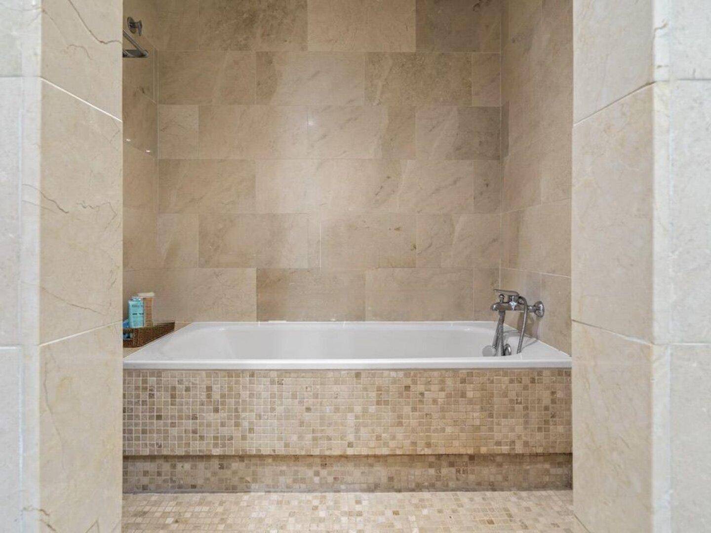 Modernes Badezimmer mit integrierter Badewanne und beigefarbenen Fliesen, inklusive Duschfunktion.