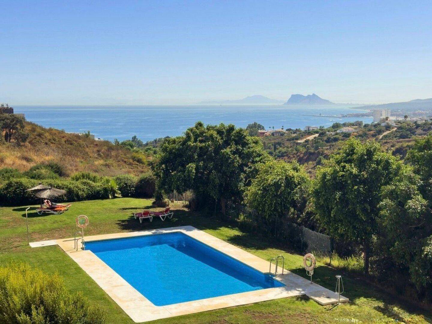 Großer Gartenbereich mit Swimmingpool, Liegestühlen und weitem Blick auf das Meer und die Küste.