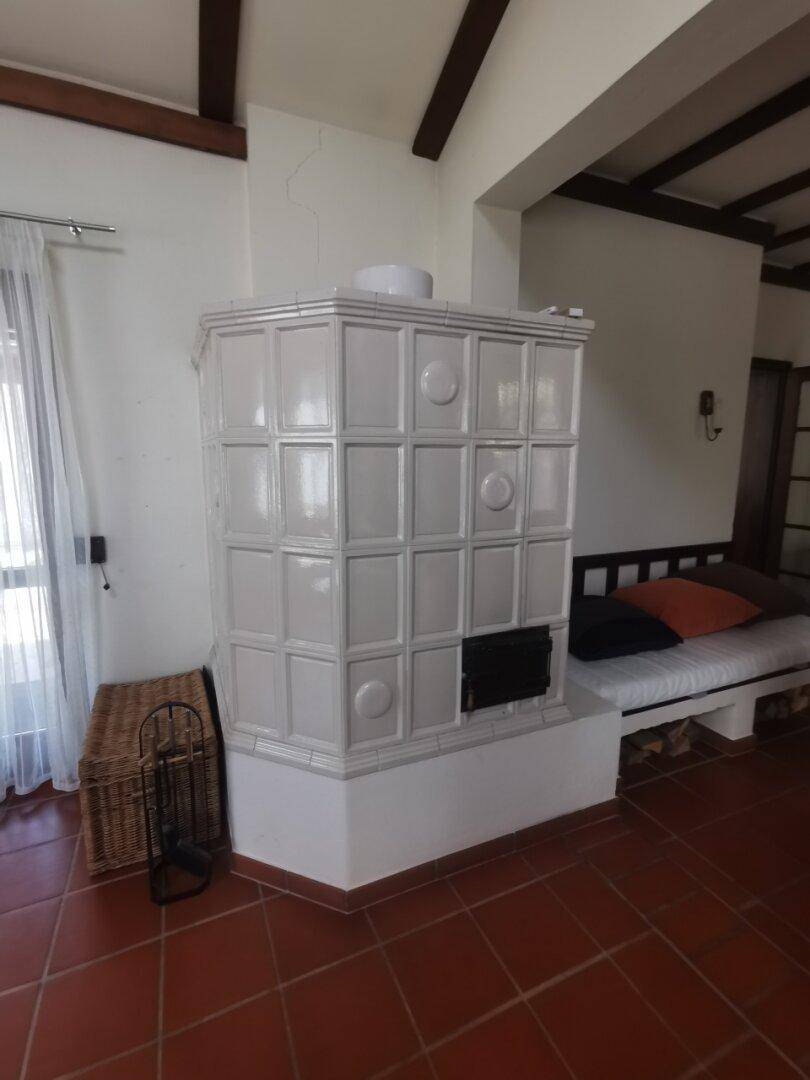 Traditioneller Kachelofen in einem gemütlichen Wohnbereich mit Terrakottafliesen und sichtbaren Holzbalken.