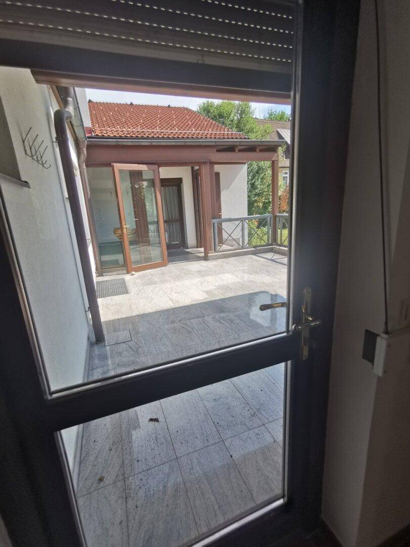 Blick von innen auf eine große, geflieste Terrasse mit Überdachung und Geländer, ideal für Entspannung.