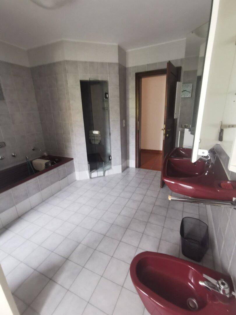 Badezimmer mit grauen Fliesen, roten Waschbecken und Bidet, sowie einer Badewanne und begehbarer Dusche.
