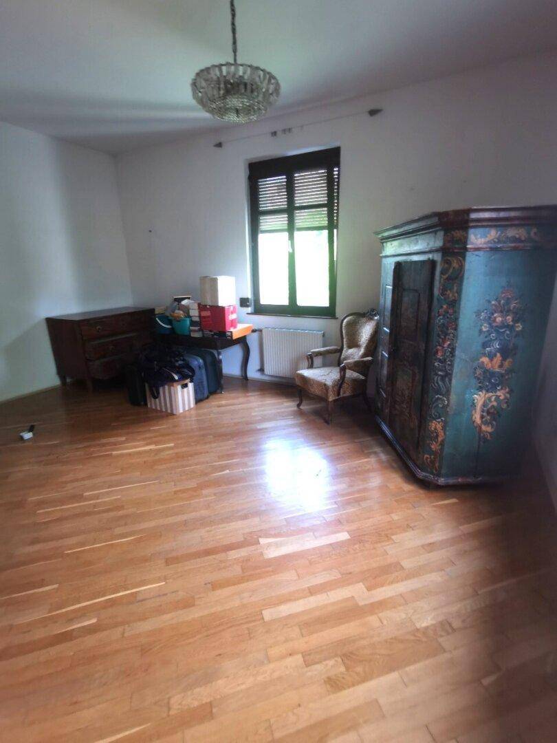 Schlafzimmer mit Holzdielenboden, einem Fenster mit dunklen Fensterläden und einem antiken Kleiderschrank.