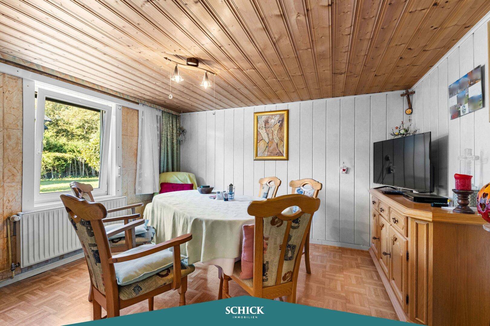 Traditioneller Essbereich mit Holztäfelung an Decke und Wänden, sowie Blick ins Grüne.