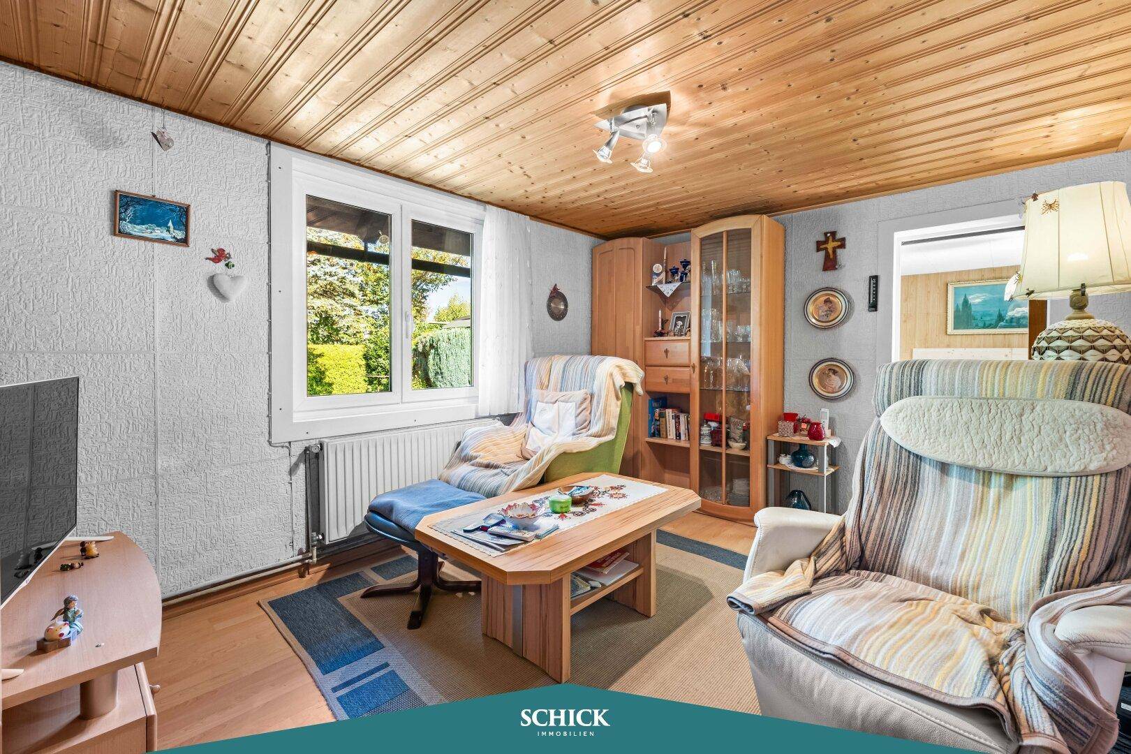 Wohnzimmer mit Holztäfelung an der Decke, gemütlichen Sesseln und Blick in den Garten.