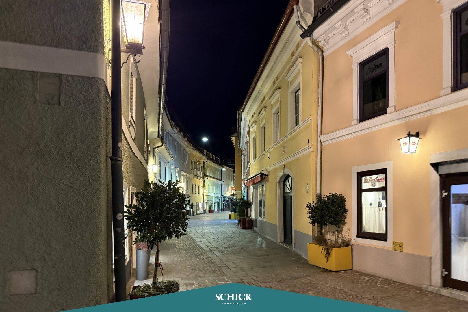 Malerische Gasse bei Nacht mit beleuchteten Gebäuden und Kopfsteinpflaster, die eine charmante Atmosphäre schafft.