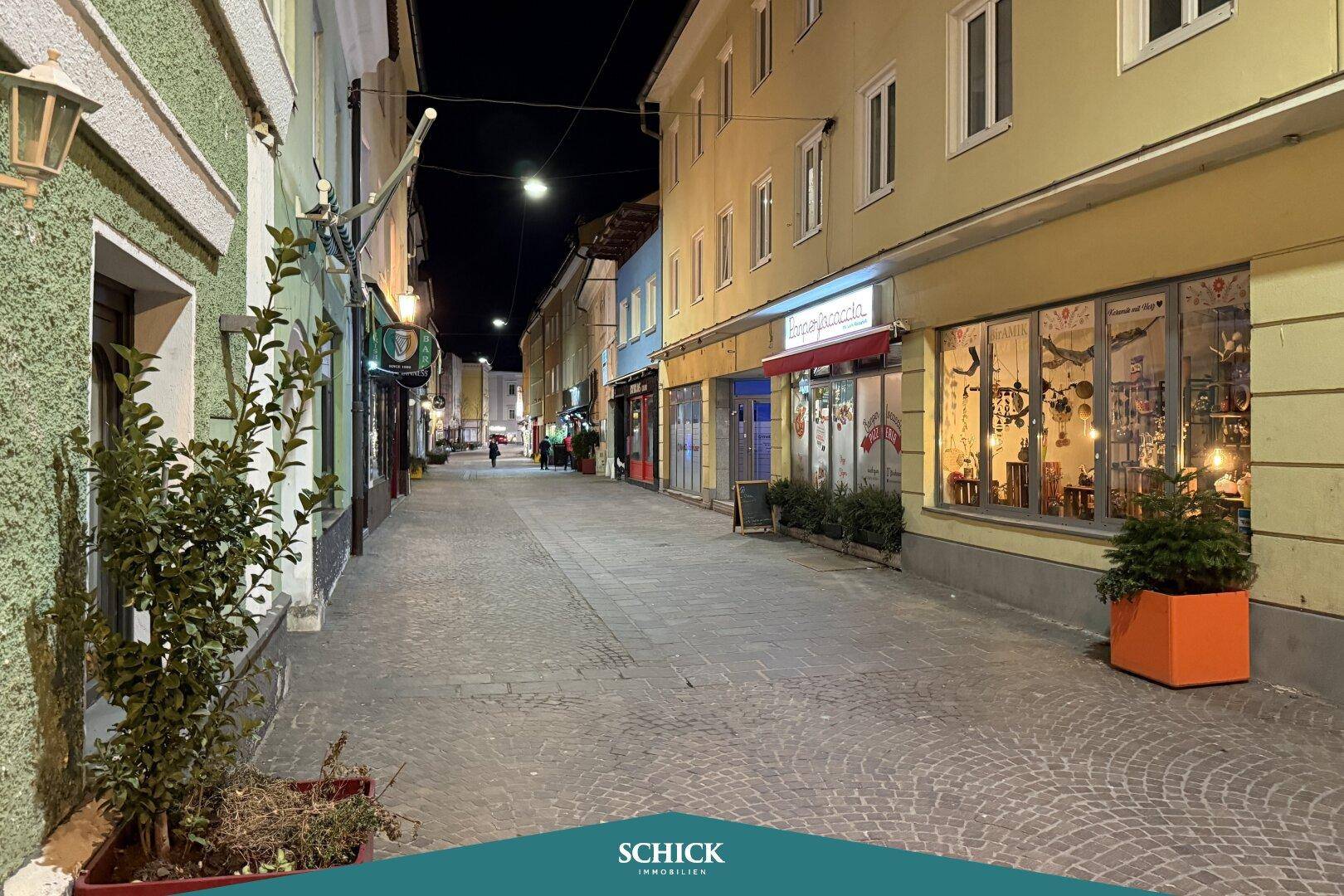Beleuchtete Straße bei Nacht mit Geschäften und Restaurants, die zum Flanieren einlädt.