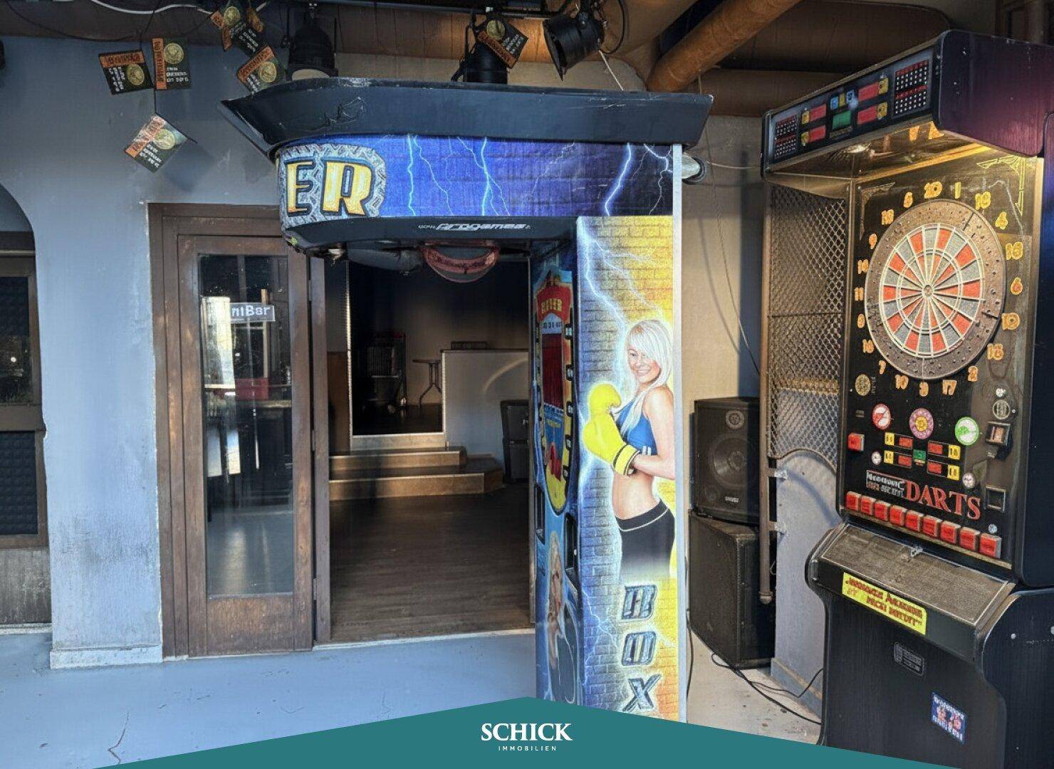 Eingang zu einem Spielbereich mit Boxautomat und Dartscheibe, der Unterhaltung bietet.