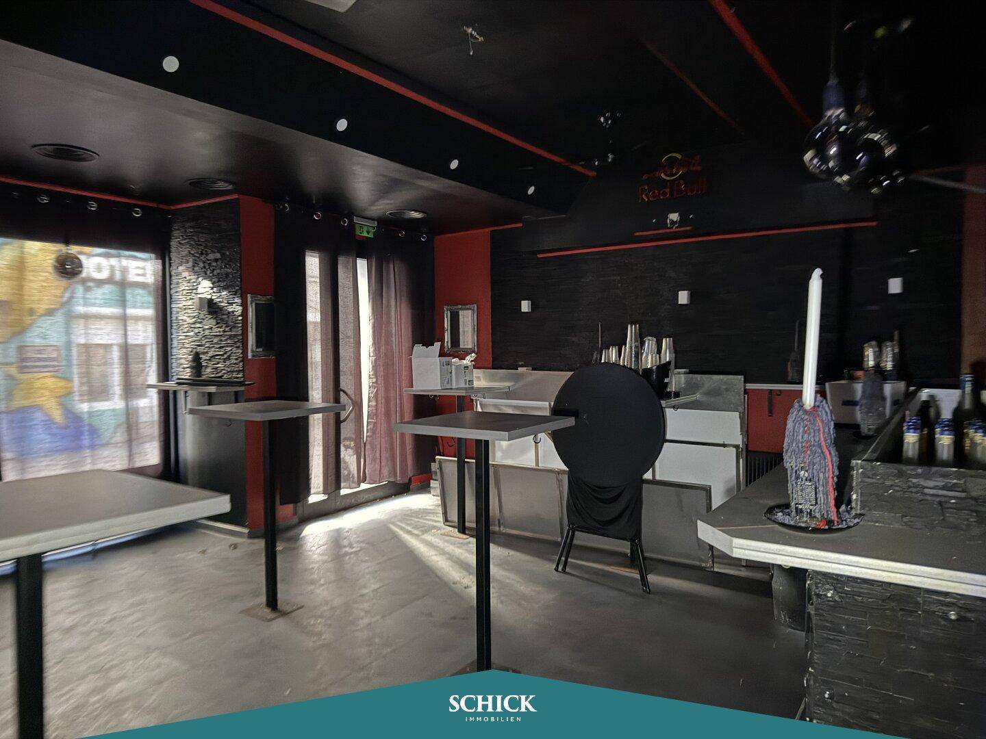 Innenansicht einer Bar mit Stehtischen, dunklen Wänden und Fenstern mit Vorhängen.