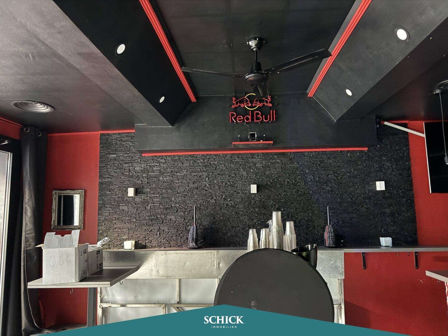 Detailansicht der Bar mit dunkler Steinwand, roten Akzenten und einem Deckenventilator.