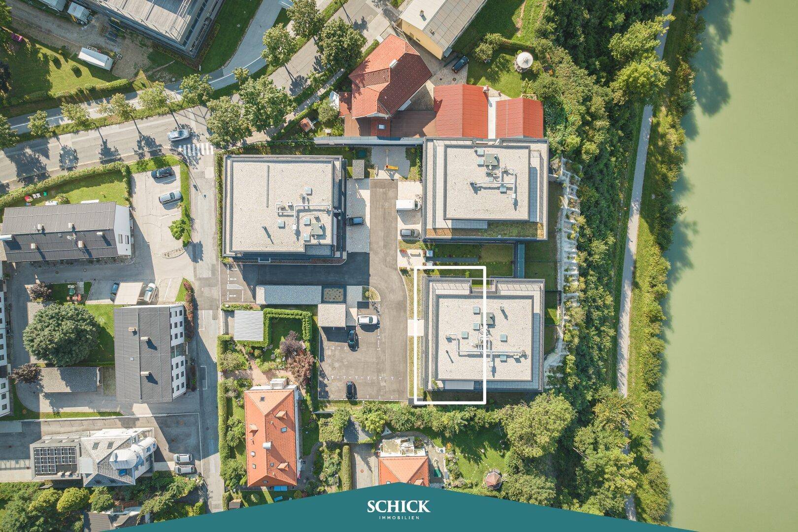 Luftaufnahme des modernen Gebäudekomplexes mit Flachdächern, Parkplätzen und Flussblick.