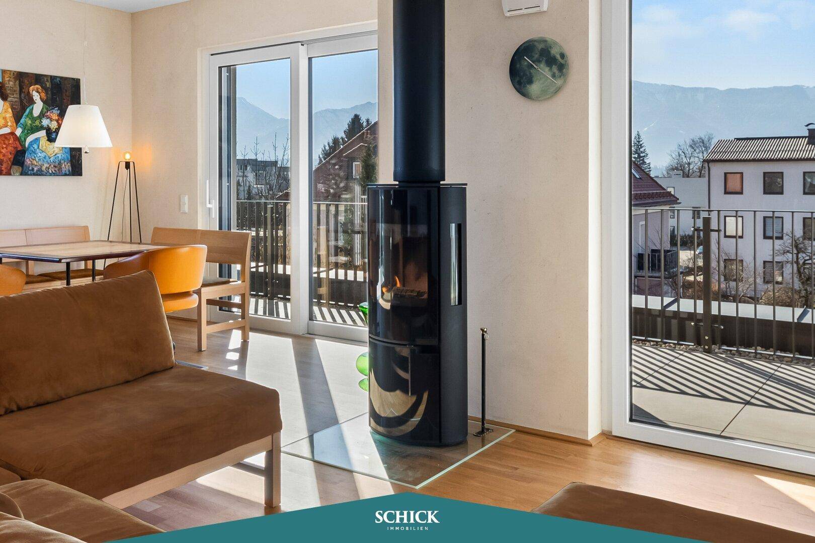 Gemütliches Wohnzimmer mit modernem Kaminofen, Holzboden und großen Fenstern mit Bergblick.