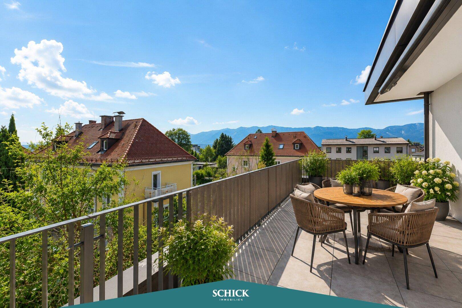Sonniger Balkon mit Rattanmöbeln und einem Tisch, der einen weiten Blick auf die Berge bietet.